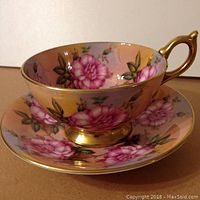 Side view of the Aynsley cup on the saucer showing rose floral design and gold painted handle.