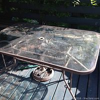 Rectangular glass top patio table showing textured pattern on the glass surface, metal frame and legs in an outdoor setting.