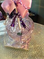 Bohemia crystal bowl with lid wrapped with pink and purple ribbon packaging, sitting on a silver glitter surface.