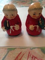 Front view of the pair of vintage ceramic Friar Monk salt and pepper shakers showing faces, red robes, and black and green books held in hands.