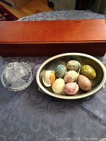 Photo of wooden tea holder closed, glass bowl with lid, and stainless steel bowl with 8 marble eggs inside on a fabric surface