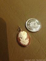 Front view of oval shell cameo pendant beside Canadian coin for scale