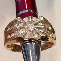 Ring viewed head-on on mandrel showing floral design with central and single-cut stones