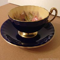 Side view of the Aynsley cup and saucer showing cobalt blue with gold handle and foot, and fruit interior.
