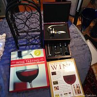 Photo of black metal wine rack, wine and liquor bottle opener set in a box, and two wine coffee table books on a table