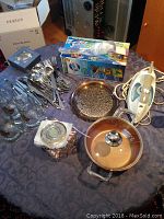 Wide shot showing all items spread on table including cutlery, glasses, pot, iron, and boxed item.