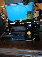 Side profile of black Singer sewing machine with gold detailing placed on wooden cabinet.