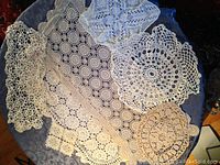 Seven varied hand knit crochet centerpieces arranged overlapping on a surface, showing different patterns and sizes.
