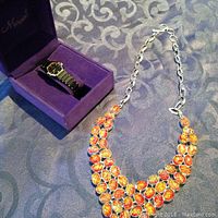 Closed-up photo of the Mervant ladies watch placed in a purple box with the fashion necklace displaying three rows of orange stones on silver-tone chain.