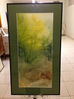 Frontal view of framed watercolor painting showing green and yellow landscape under glass in black frame with green matte.