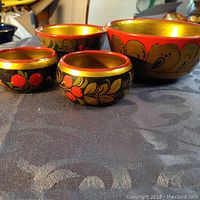 Four handcrafted Russian Khokhloma wooden bowls in red, black, and gold lacquer. The bowls vary in size and are decorated with traditional floral and berry motifs.