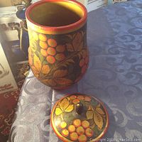 Photo of a Russian Khokhloma style wooden container with lid showing traditional red, black, and gold hand-painted decoration with berries and leaves.