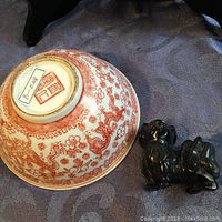 Porcelain bowl (upside down) and soapstone dog figurine displayed together on patterned fabric.