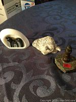 Photo showing three small stone sculptures on patterned cloth: abstract green serpentine, beige resting animal, and polished serpentine bull figurine on rough base.