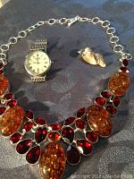 Full view of the watch, necklace, and pendant earring on dark fabric surface.