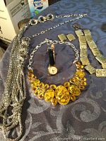 Full lot view showing silver-tone multi-strand necklace with tassels, yellow amber-toned statement necklace, gold-tone linked necklace and earrings, and small wristwatch.
