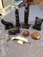 Photo showing a group of 10 assorted figurines including carved animals, birds, decorative nut carvings, and glass figures on a cloth surface.