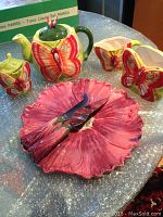 Photo of the porcelain tea set including teapot, creamer, sugar bowl with butterfly design and matching pink cake tray with three utensils.