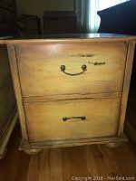 Front view of rustic country style wooden night table showing two drawers with bronzed metal bail pulls and bun feet.