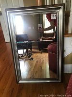 Full view of the rectangular mirror standing on floor reflecting room interior with visible furniture.