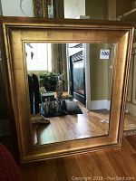 Front view of the framed rectangular mirror showing the gold-toned wooden frame and beveled mirror surface reflecting a room interior.
