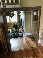 Full view of large rectangular beveled wall mirror with ornate gold-toned wooden frame, reflecting room.