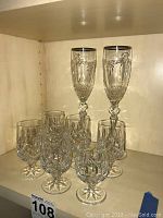 Two Waterford 2000 crystal flutes with silver-plated lip rims behind six crystal stem glasses etched with 'PREMIER'. All pieces clearly visible on a wood shelf.