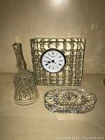 Waterford clock, crystal bell, and oval candle holder arranged on table.