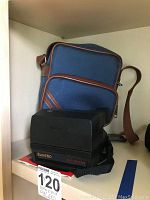Polaroid Sun 660 camera with blue and brown carrying bag behind it, showing overall lot contents.