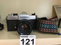 Front view of Yashica TL Electro film camera with lens and patterned strap alongside it.