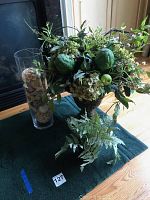 Overall photo showing the two faux floral arrangements and cylinder vase arranged on a table in front of a fireplace.