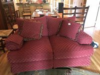 Wide front view of the red patterned loveseat with two square throw pillows and arm covers on each armrest, sitting in a dining room setting.