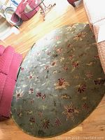 Photo showing entire round rug with multicolor floral design, placed on wooden floor between red seating furniture.