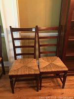 Two solid wood ladder back chairs with woven rush seats placed side by side on wood floor.