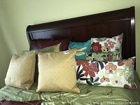 Ten assorted throw pillows on bed showcasing different shapes and floral fabric patterns