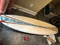 Full view of BIC surfboard showing floral and geometric stripes design along center, surface discoloration visible.