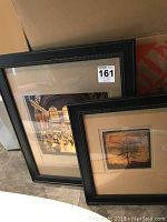 Two framed photographs leaning against a wall; one larger, one smaller.