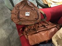 Leather backpack and brown leather duffel bag on red chair and table surface