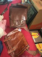 Photo showing a brown leather backpack and a brown leather shoulder briefcase on a red surface.