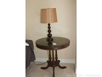 Full view of the vintage round wood table with a single lamp on top, showing the overall shape, color, and design of the table and lamp.