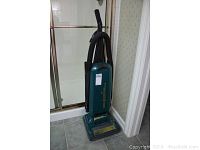 Full view of an upright green Eureka Powerline Plus vacuum next to the shower door and part of bathroom floor showing tiles.