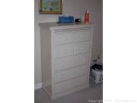 Front-left angled view of the taller dresser showing five drawers and decorative trim with items on top.