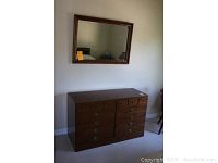 Ethan Allen dresser with mirror hung above on wall. Dresser has wood finish and several drawers with brass handles.
