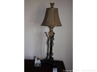 Decorative lamp with metal base and fabric lampshade, boy and girl ceramic figurine sitting beside it