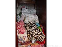 Stack of folded kitchen linens including patterned towels and cloths such as red, zebra print, floral, and white linens