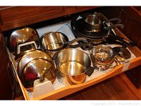 Drawer open showing stainless steel saucepans and pots with lids together with black Teflon non-stick frying pans and skillets, and stainless steel steamer basket.