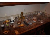 Wide view of multiple items on countertop including glassware, brass items, wooden trays, creamer, teapot, and decorative pieces