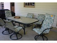 Wide view of the entire patio dining set including the glass-top table and six swivel chairs with floral cushions around it.