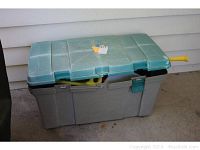 Closed view of large gray plastic patio storage box with blue lid, partially revealing contents inside
