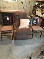 The full set of items showing the brown La-Z-Boy recliner between two folding wood chairs with fabric seats, items placed on a concrete floor in a basement room.